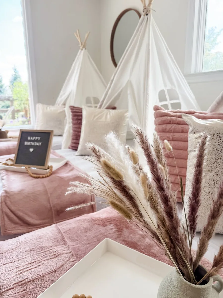 Close-up of a Boho sleepover teepee setup with pampas grass, blush velvet blankets, and a Happy Birthday letter board