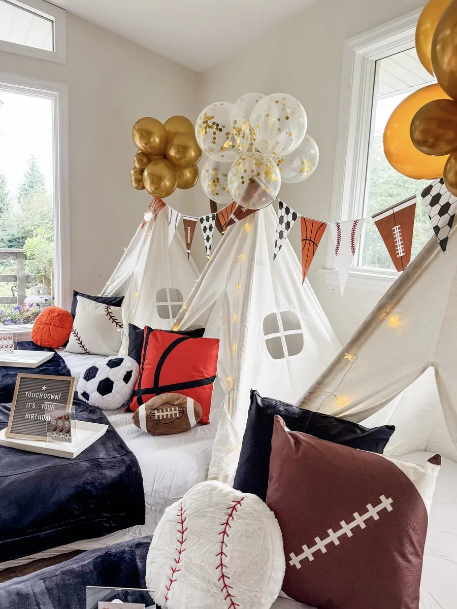 Close-up of a Sports sleepover setup with a Touchdown It's Your Birthday letter board, soccer and baseball pillows, and a gold and confetti balloon garland