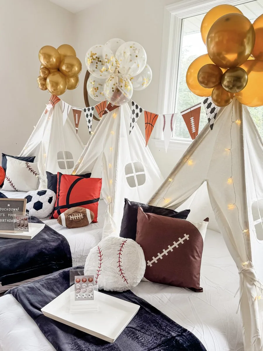 Sports-themed decorative throw pillows including baseball, football, basketball, and soccer on a teepee bed