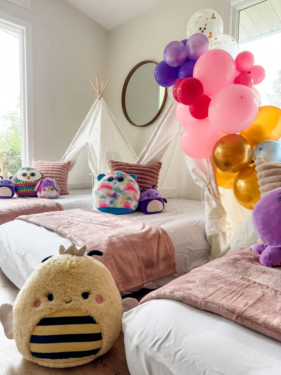 Squishmallow-themed teepee sleepover with a colorful balloon arch and plush characters resting on each bed