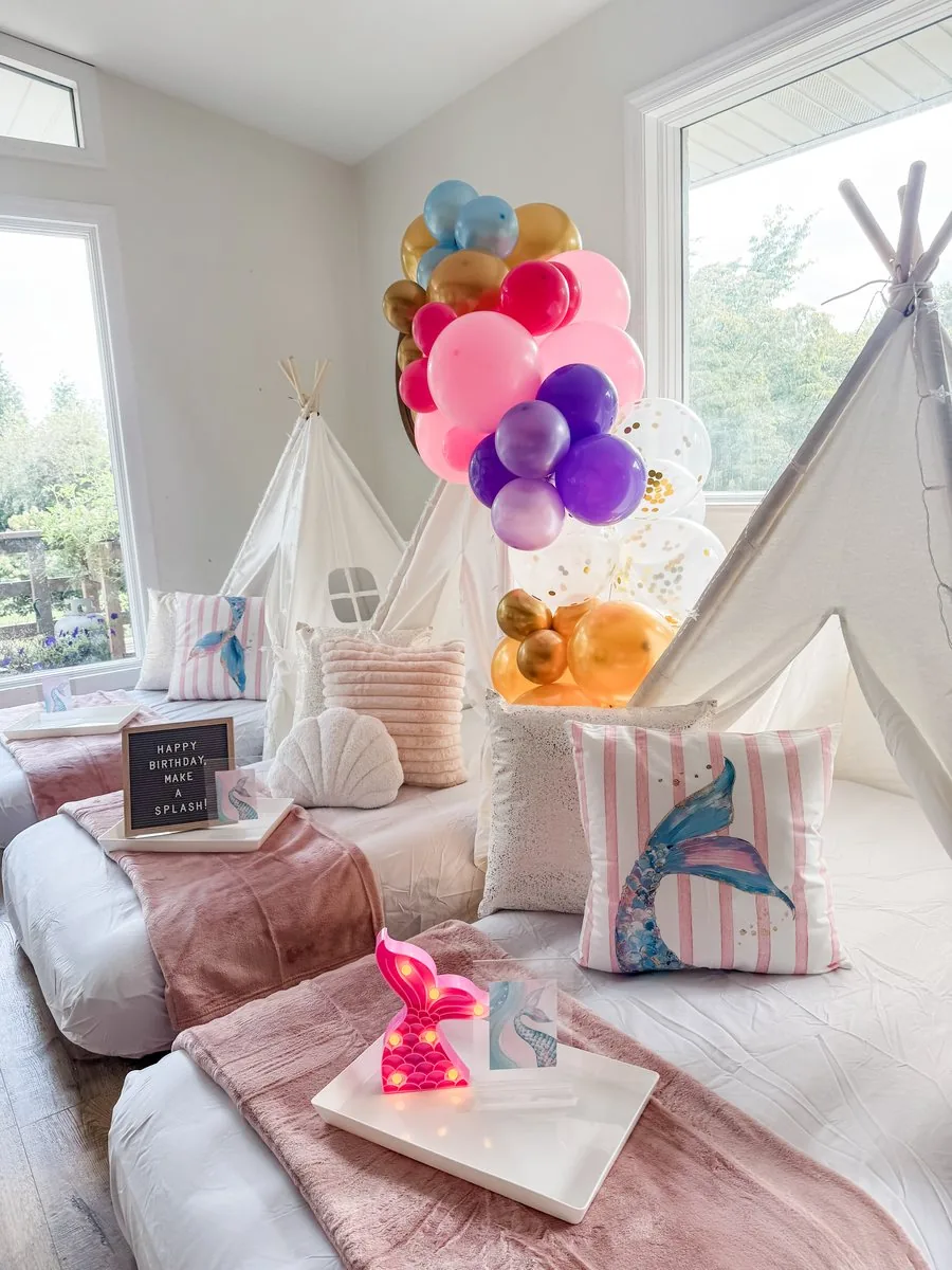 Twin air mattresses made up with fitted sheets and blush throw blankets in a mermaid-themed teepee setup
