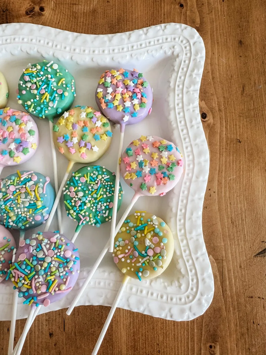 Two dozen pastel cake pops with colorful sprinkles on a white platter